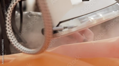 Young women uses steam to iron her orange clothes. Slow motion. photo