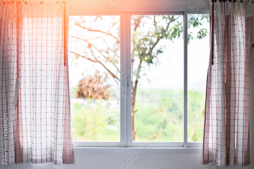 Sunlight through in room open curtains with balcony and nature tree on outside window - bedroom window in the morning