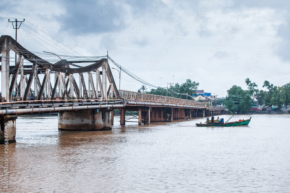 Khmer fishermen steering old fishing boat past under the ancient bridge. Khmer fishermen steering old fishing boat past under the ancient bridge.