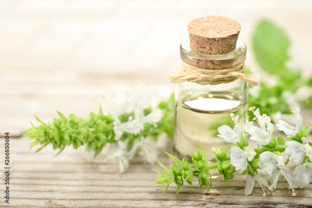 basil essential oil in the glass bottle, with fresh flowers, on the wooden board