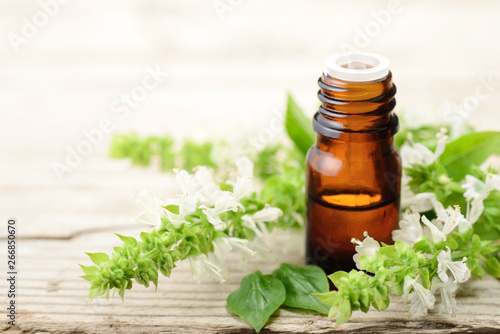 basil essential oil in the amber glass bottle, with fresh flowers, on the wooden board
