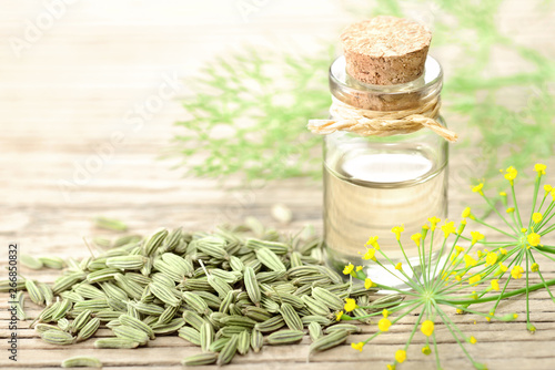 fennel essential oil in the glass bottle, with seeds and flowers, on the wooden board