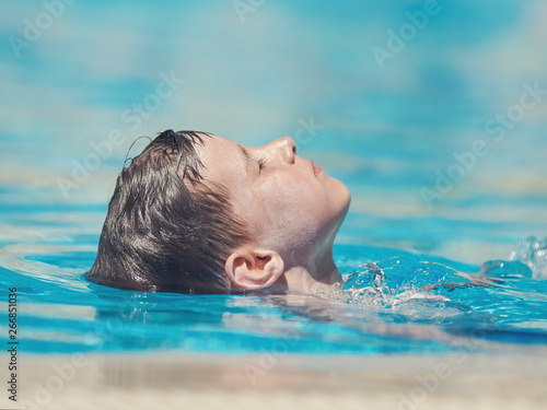 Cute European boy swimming backstroke in pool.