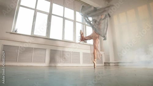 Expressive video of female ballet dancer dressed in grey-blue flowing fabric spinning on one leg on white background.