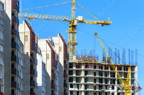 Finished Apartment Building and a New High-Rise Building Construction Site with Yellow Cranes against Blue Sky. Real Estate, Residential Buildings Urban Mixed-Use Development Concept.