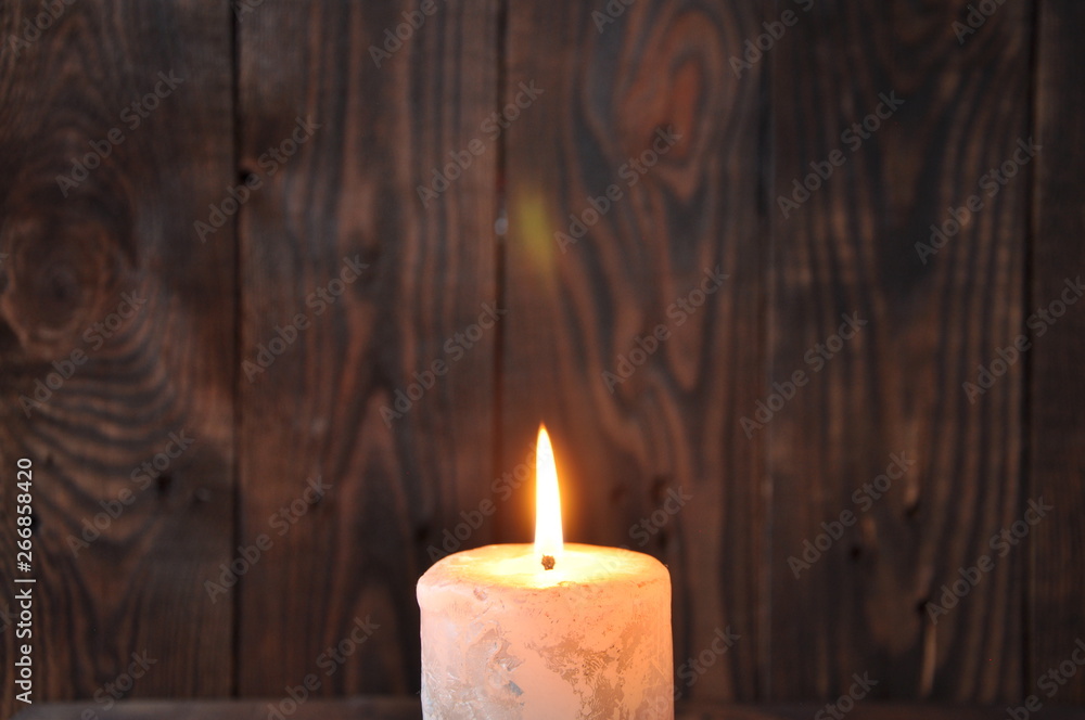 a large candle burns in the darkness on a wooden texture background