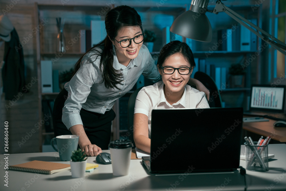 Fototapeta premium woman entrepreneur working on laptop with colleague in office. group of asian female business partners working late night to meet project deadlines. lady coworkers done plan smiling joyful check