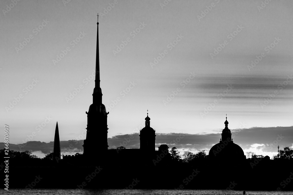 Naklejka premium The black and white silhouette of Peter and Paul Fortress in St. Petersburg, Russia in the rays of setting sun on the background of cloudy sky 
