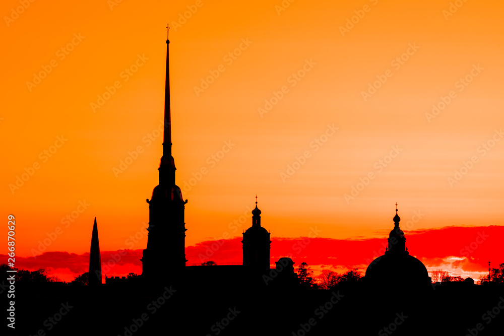 The black silhouette of Peter and Paul Fortress in St. Petersburg, Russia in the rays of setting sun on the yellow, orange and red background of cloudy sky 