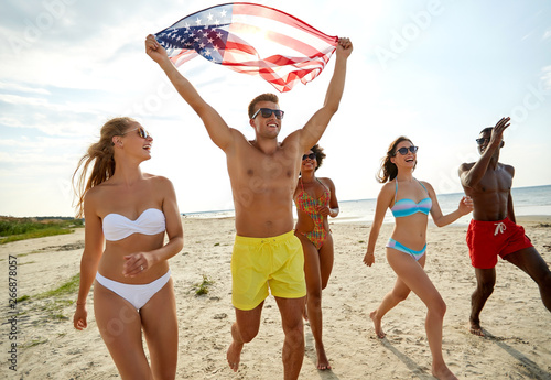 independence day, summer holidays and people concept - group of happy friends with american flag on beach celebrating 4th of july