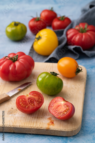 verschiedene Tomaten teilweise angeschnitten auf holzbrett und hellem untergrund hochformat