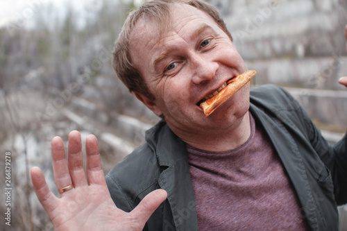 The man is going to eat pizza. It's in the open air. Holding a piece of pizza in hand, portrait