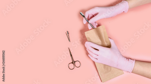 packing a manicure tool in kraft packages before sterilizing in a dry oven. Manicure tool in the hands of the master isolated on pink background. Close up