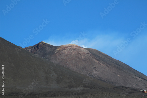 The black lava ash of smoking volcano Etna against blue sky, Sicily, Italy