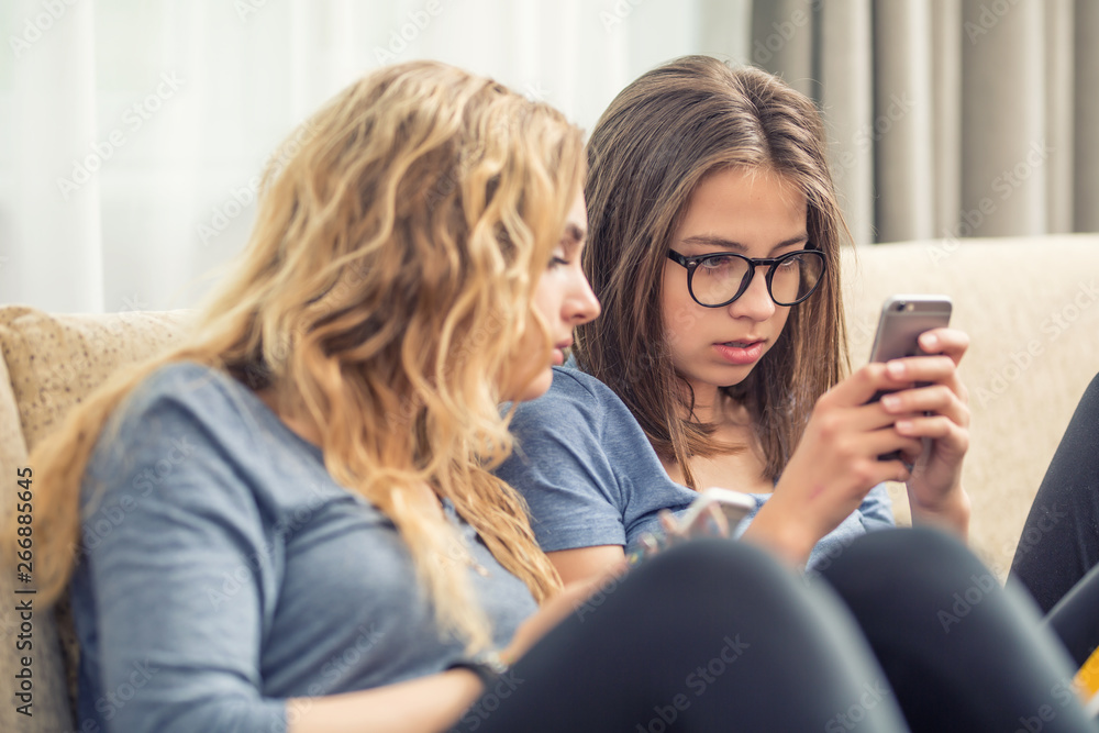 Two teen girs or sisters using smart phones in the living room