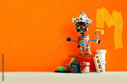 Funny decorator robot repaints the wall of the room orange color. Creative painter robot toy, wooden stepladder and interior redecoration tools, paint buckets rollers. Copy space