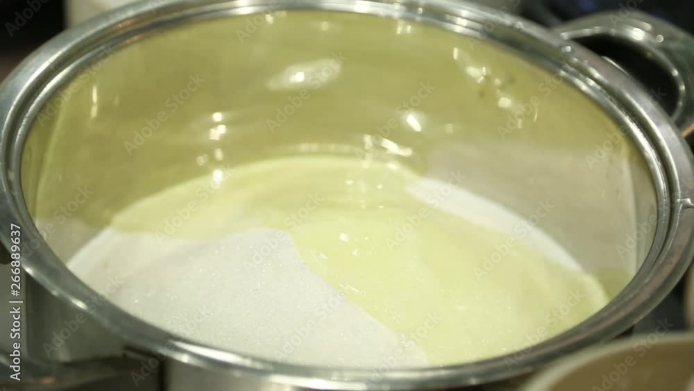 yellow syrup is poured into a metal saucepan with sugar slowly from a spoon. large yellow syrup is poured into a metal saucepan with sugar slowly from a spoon. large