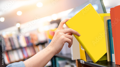 Bestseller publishing concept. Male hand choosing and picking yellow book from wooden bookshelf in bookstore. Education research in university public library. photo