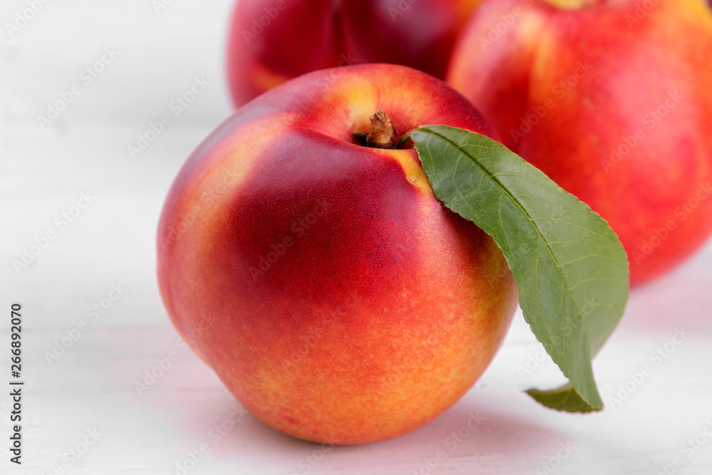 Ripe large nectarines with a green leaf close-up on a white wooden background Ripe large nectarines with a green leaf close-up on a white wooden background
