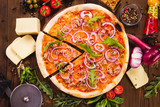 Italian pizza with chicken, onions and rucola leaves on a dark wooden background with ingredients around (close top view). Cut one piece