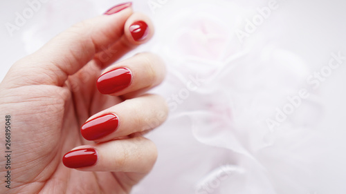 Φωτογραφία Beautiful female hand with red nails against the background of a white wedding b