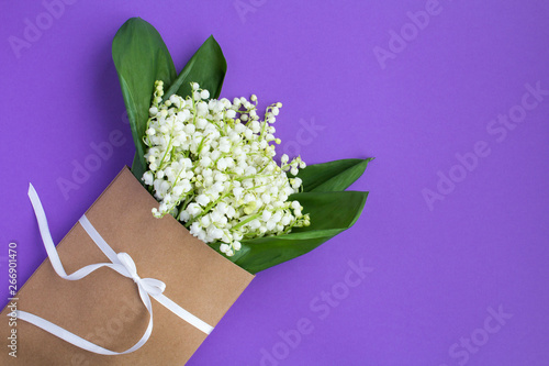 Lilies of the valley in a envelope tied with a white ribbon on the lilac background.Top view.Copy space.Spring flowers concept.