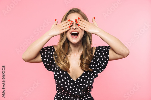Happy young pretty woman posing isolated over pink wall background covering eyes.