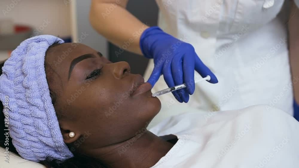 Side view of cosmetologist hands making beauty injection for young african woman. Side view of cosmetologist hands making beauty injection for young african woman.