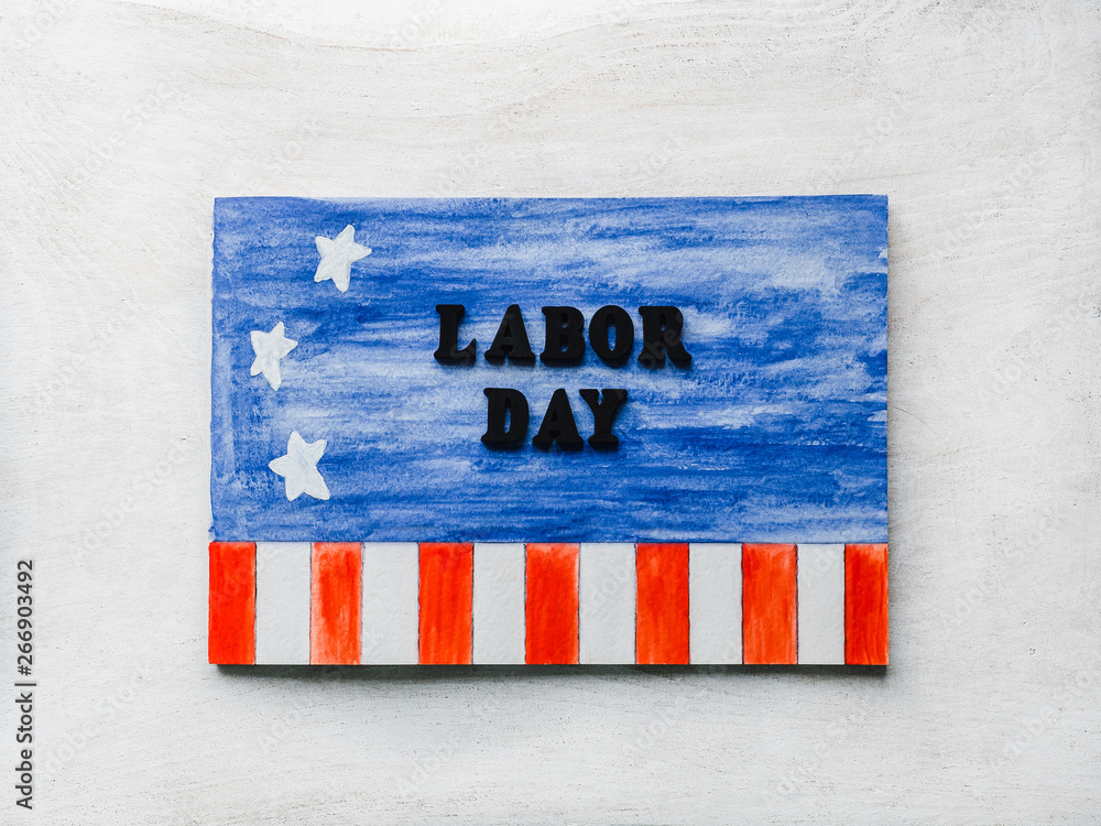 Obraz premium LABOR DAY. Notepad, American flag pattern and wooden letters of the alphabet on a white table. Close-up. Bright photo and space for your inscriptions. Congratulations to relatives, friends, colleagues