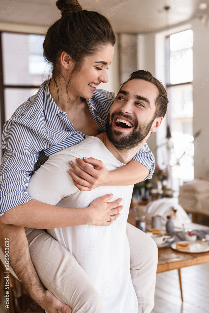 © Drobot Dean - Photo of playful brunette couple in love smiling while hugging together in apartment