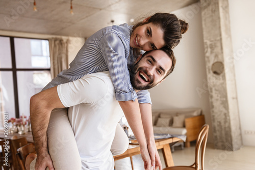 Photo of cute brunette couple in love smiling while hugging together in apartment