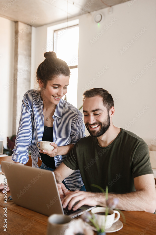 Image of pleased brunette couple working on laptop together while sitting at table at home Image of pleased brunette couple working on laptop together while sitting at table at home