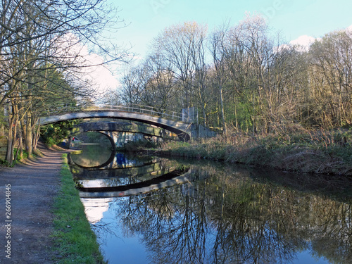 two bridges crossing the leeds to liverpool canal in armley with trees reflected on the water and footpath photo