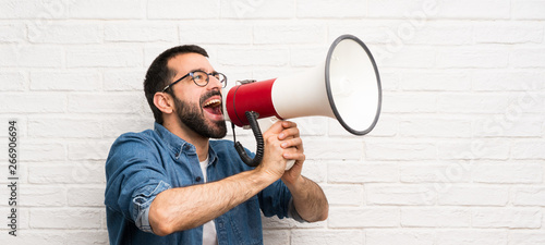 Handsome man with beard over white brick wall shouting through a megaphone photo