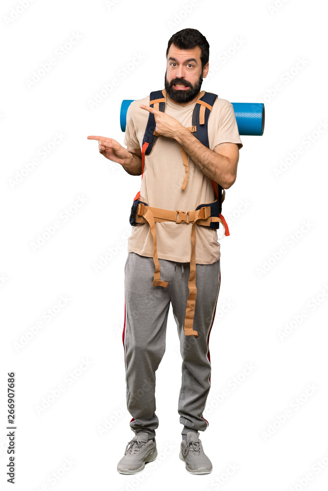 Hiker man frightened and pointing to the side over isolated white background Hiker man frightened and pointing to the side over isolated white background