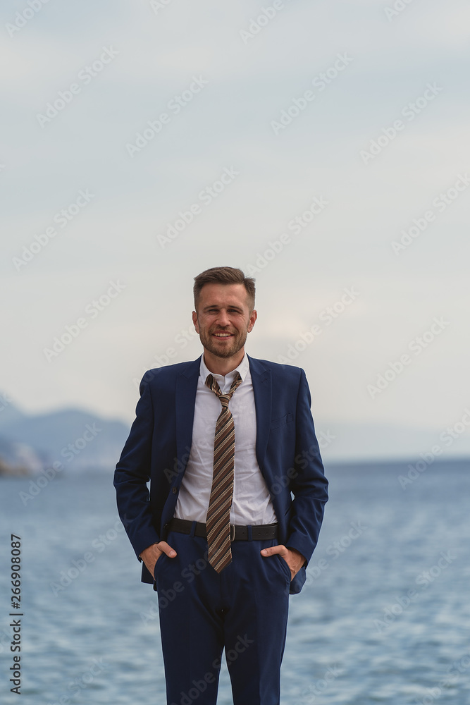 Businessman standing on the beach in a suit a untied tie. He looks at the camera and laughs, he is happy