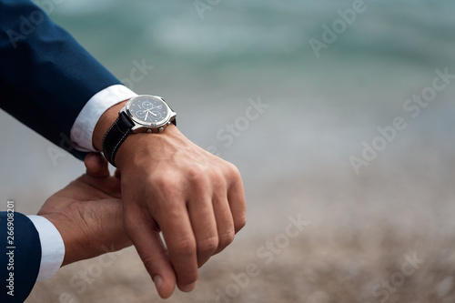 A man in a business suit checking a wrist watch on his hand on background sea