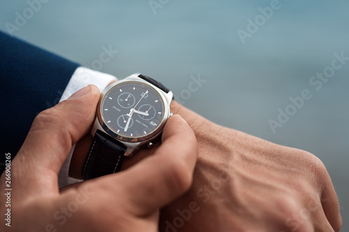 A man in a business suit checking a wrist watch on his hand on background  sea