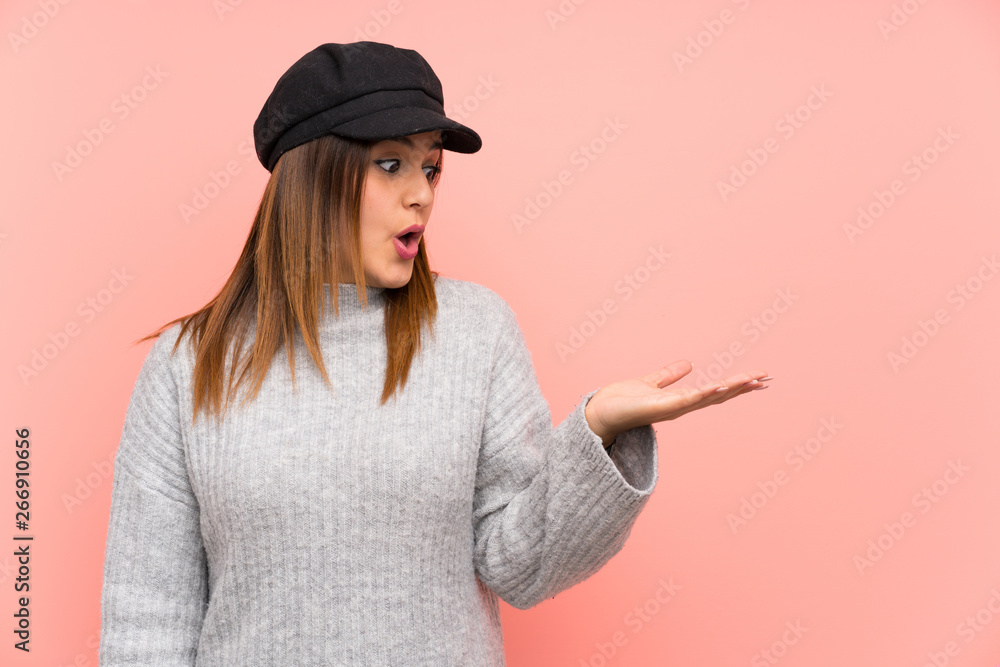 Fashion woman with hat over pink wall holding copyspace imaginary on the palm Fashion woman with hat over pink wall holding copyspace imaginary on the palm