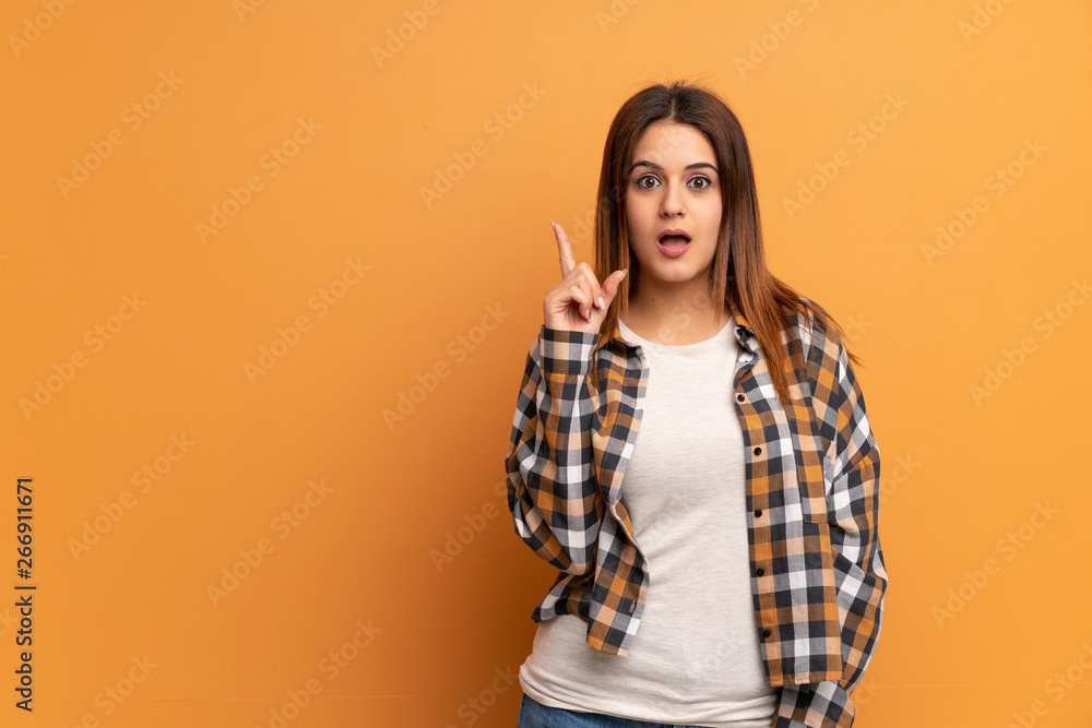 Young woman over brown wall thinking an idea pointing the finger up Young woman over brown wall thinking an idea pointing the finger up