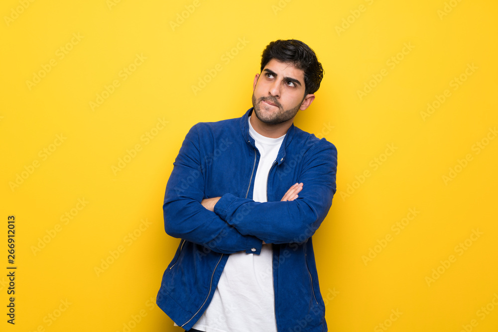 Man with blue jacket over yellow wall with confuse face expression Man with blue jacket over yellow wall with confuse face expression