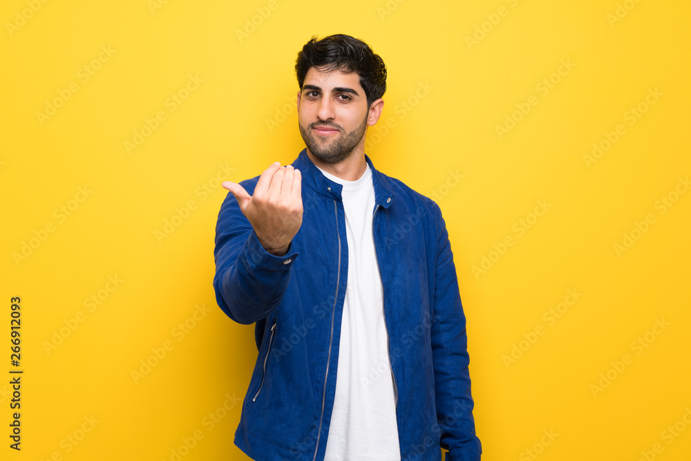 Man with blue jacket over yellow wall inviting to come with hand. Happy that you came Man with blue jacket over yellow wall inviting to come with hand. Happy that you came