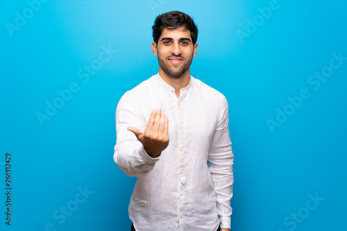 Foto Young man over isolated blue wall inviting to come with hand