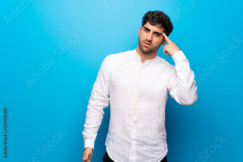 Young man over isolated blue wall making the gesture of madness putting finger on the head © luismolinero