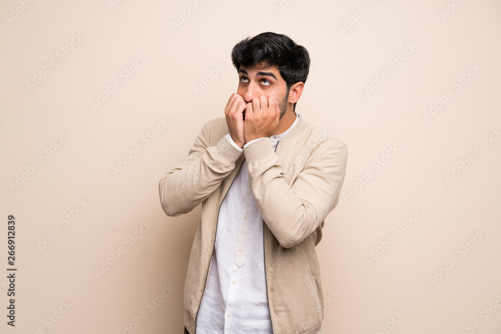 Young man over isolated wall nervous and scared putting hands to mouth Young man over isolated wall nervous and scared putting hands to mouth