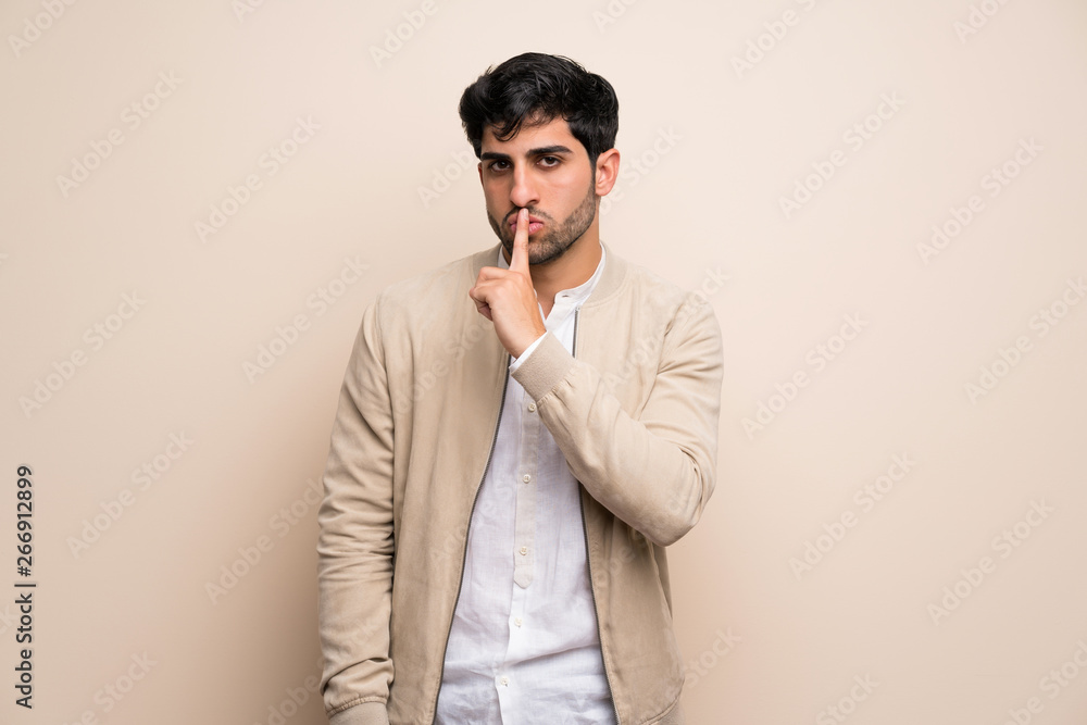 Young man over isolated wall showing a sign of silence gesture putting finger in mouth Young man over isolated wall showing a sign of silence gesture putting finger in mouth