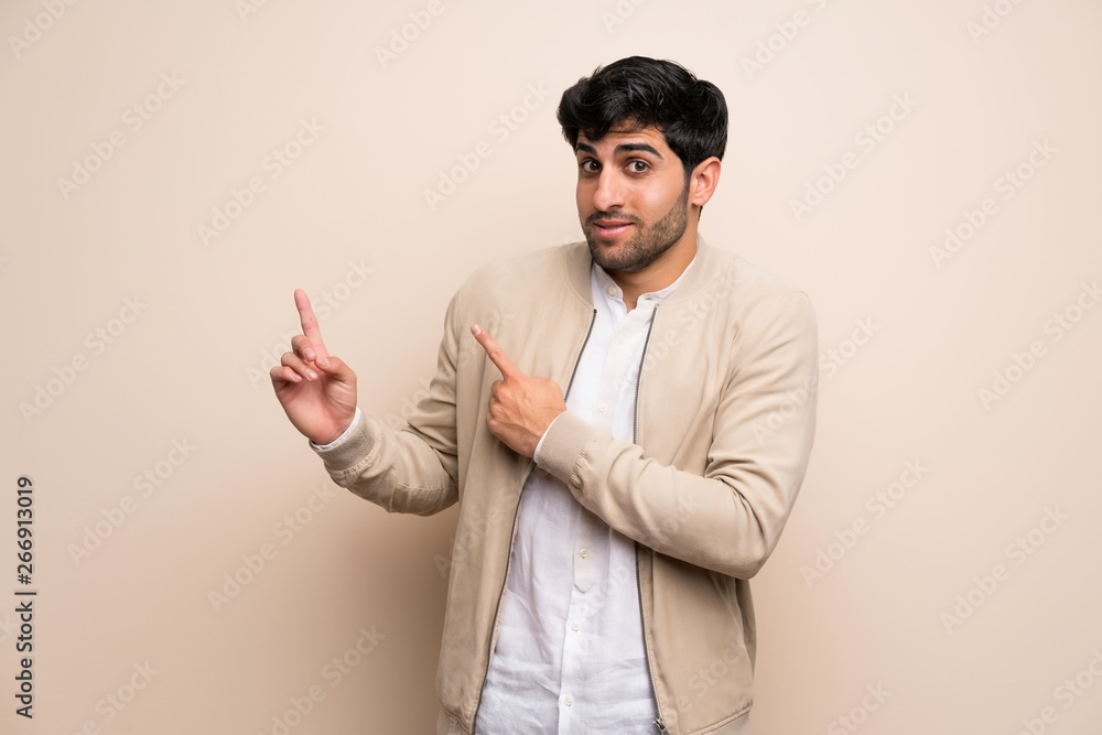 Young man over isolated wall frightened and pointing to the side Young man over isolated wall frightened and pointing to the side