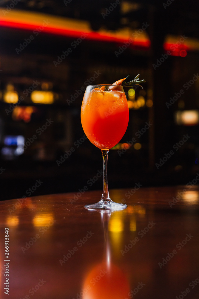 A refreshing cold orange cocktail or lemonade with ice, garnished with orange peel and rosemary, served in a wine glass. Shot in the bar, studio light. A refreshing cold orange cocktail or lemonade with ice, garnished with orange peel and rosemary, served in a wine glass. Shot in the bar, studio light.