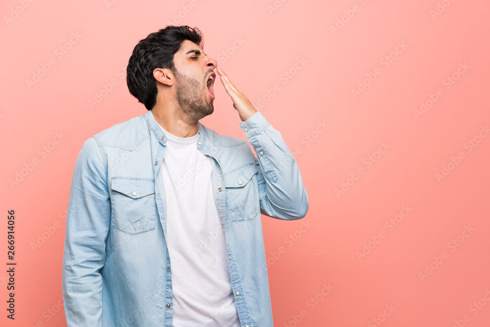 Young man over pink wall yawning and covering wide open mouth with hand Young man over pink wall yawning and covering wide open mouth with hand