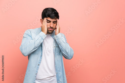 Young man over pink wall with headache